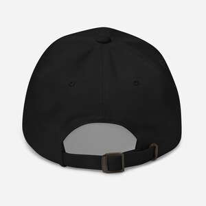 May include: A solid black baseball cap featuring a six-panel construction with a button on the crown. The back of the cap includes an adjustable fabric strap with a metallic buckle closure, allowing for a customizable fit for various head sizes.