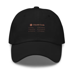 May include: A black baseball cap featuring a small orange sun icon and the text Claude Code followed by a list of six terms: Vibing, Noodling, Thinking, Percolating, Ruminating, and Wrangling, each preceded by a small orange dot.