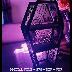 Puede incluir: Una estantería negra con forma de ataúd que presenta intrincados recortes de telaraña en los paneles laterales y dos estantes horizontales. El texto en la parte inferior dice DIGITAL FILE - SVG - DXF - PDF. Es un archivo digital.