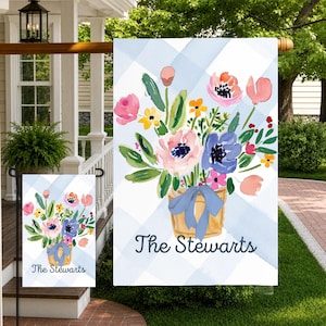 Peut inclure: Un drapeau de jardin rectangulaire avec un fond à carreaux vichy bleu clair et blanc. Au centre, un bouquet de fleurs roses, jaunes et bleues à l'aquarelle dans un pot beige avec un ruban bleu. Le texte "The Stewarts" est imprimé en dessous.