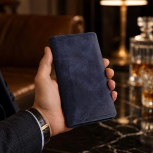 May include: A rectangular navy blue wallet with a matte, textured finish and visible stitching along the edges. The wallet is held in a vertical position, showcasing its slim profile and uniform dark blue color throughout the exterior surface.