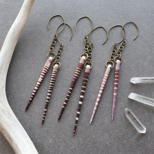 May include: Three pairs of earrings with long, thin, striped, seashell pendants. The earrings are made with brass chains and hooks. The seashells are a mix of pink and brown.