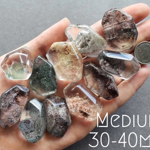 May include: A collection of 10 clear quartz crystals with inclusions of various colors, including green, brown, and gray. The crystals are faceted and have a natural, rough texture. The crystals are approximately 30-40 mm in size.  MEDIUM: 30-40MM