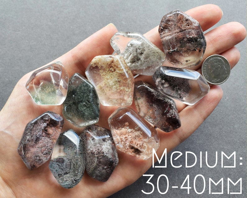 May include: A collection of 10 clear quartz crystals with inclusions of various colors, including green, brown, and gray. The crystals are faceted and have a natural, rough texture. The crystals are approximately 30-40 mm in size.  MEDIUM: 30-40MM
