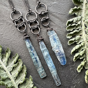 Peut inclure: Trois colliers avec des pendentifs en cristal de kyanite bleue et des maillons de chaîne argentés. Les chaînes sont composées de plusieurs anneaux reliés.
