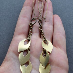 May include: Gold tone dangle earrings with a chain and three leaf-shaped charms.
