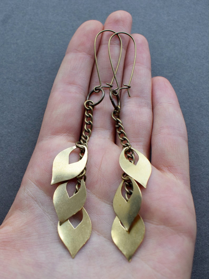 May include: Gold tone dangle earrings with a chain and three leaf-shaped charms.