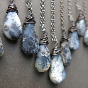 Puede incluir: Una colecci&oacute;n de colgantes de &oacute;palo dendr&iacute;tico en forma de l&aacute;grima, cada uno envuelto en alambre de cobre oscuro y suspendido de una cadena de metal a juego. Las piedras tienen una base blanca lechosa con inclusiones oscuras.