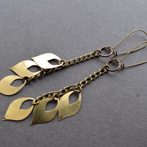 May include: A pair of gold-toned earrings with a chain and multiple leaf-shaped charms. The earrings are made of metal and have a simple, elegant design.