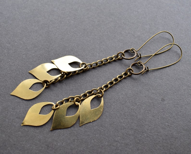 May include: A pair of gold-toned earrings with a chain and multiple leaf-shaped charms. The earrings are made of metal and have a simple, elegant design.