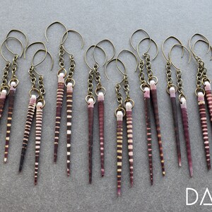 May include: A set of eight pairs of earrings featuring long, thin, striped shells with a brown and white pattern. Each pair is attached to a gold chain and a gold hook.
