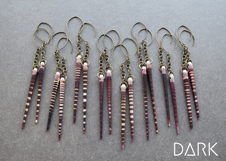 May include: A set of eight pairs of earrings featuring long, thin, striped shells with a brown and white pattern. Each pair is attached to a gold chain and a gold hook.