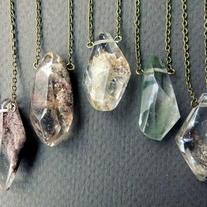 May include: Five crystal pendants on brass chains. The crystals are clear with inclusions of brown, gray, and green. The pendants are all different shapes and sizes.