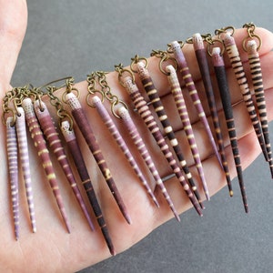 May include: A pair of earrings with multiple strands of purple and white striped seashells hanging from a brass chain.