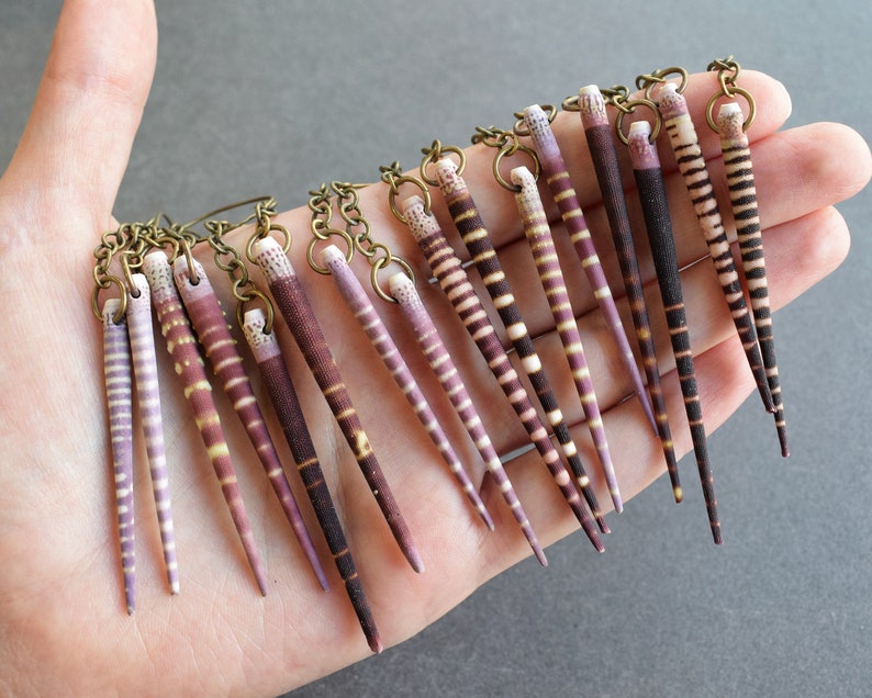 May include: A pair of earrings with multiple strands of purple and white striped seashells hanging from a brass chain.
