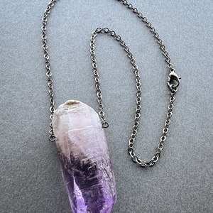 May include: A silver chain necklace with a large, purple amethyst crystal pendant.