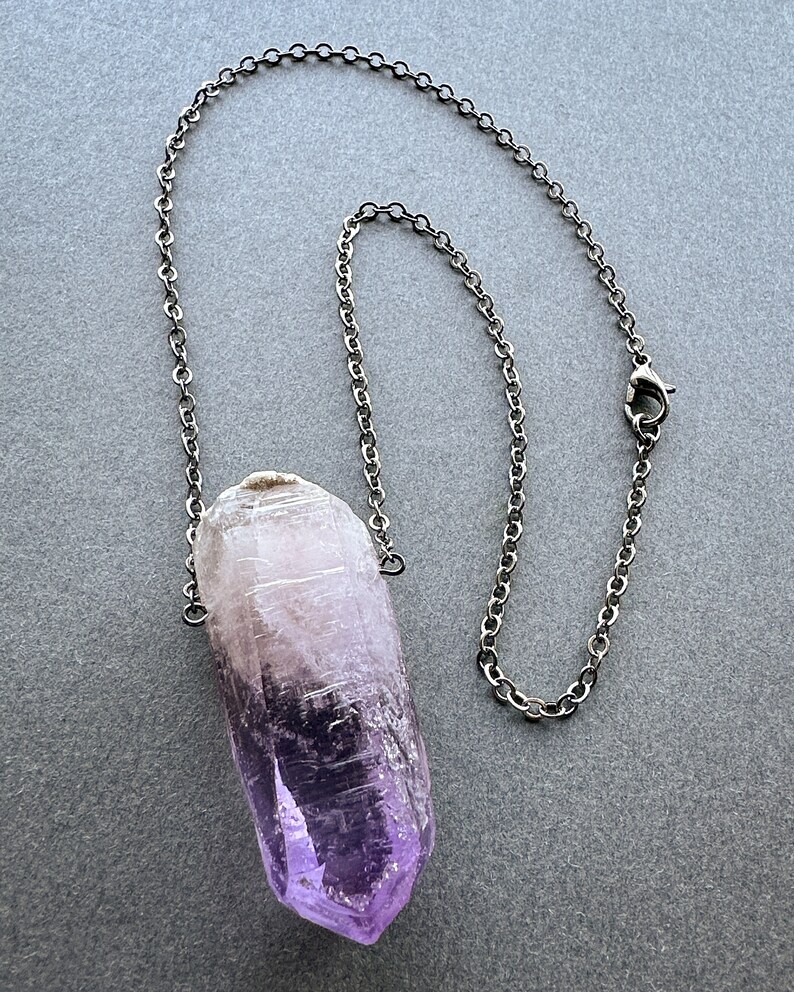 May include: A silver chain necklace with a large, purple amethyst crystal pendant.