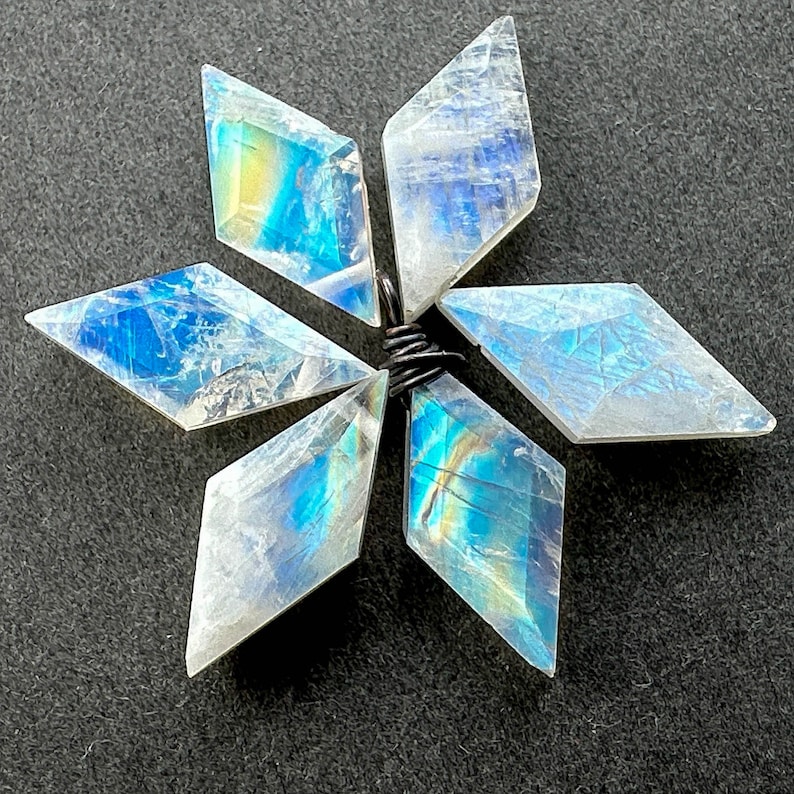 K&ouml;nnte beinhalten: Ein sechszackiger Stern aus schimmerndem Regenbogen-Mondstein, jede Spitze hat eine Diamantform, der Stern ist mit Silberdraht verbunden.