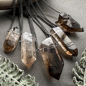 May include: A set of seven smoky quartz crystal pendants on delicate silver chains. The crystals are all different shapes and sizes, and they have a beautiful, smoky brown colour.