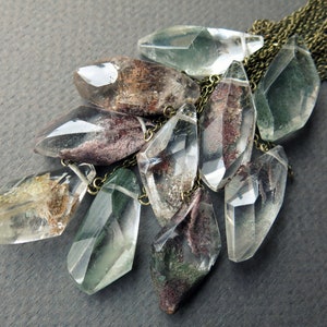 May include: A necklace with a cluster of green, brown, and clear crystal pendants hanging from a brass chain.