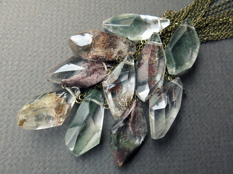 May include: A necklace with a cluster of green, brown, and clear crystal pendants hanging from a brass chain.