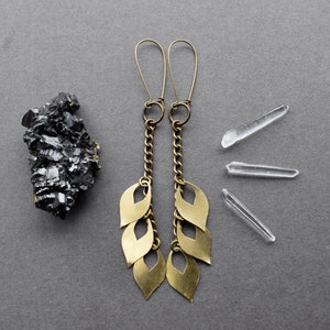 May include: A pair of gold dangle earrings with a chain and multiple leaf-shaped charms. The earrings are on a gray background.