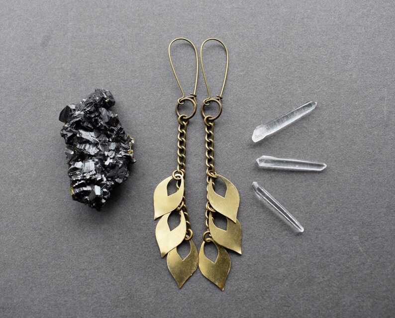 May include: A pair of gold dangle earrings with a chain and multiple leaf-shaped charms. The earrings are on a gray background.