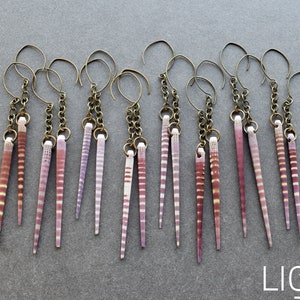 May include: A set of 10 earrings featuring pairs of long, thin, pink and white striped seashells hanging from gold chains.