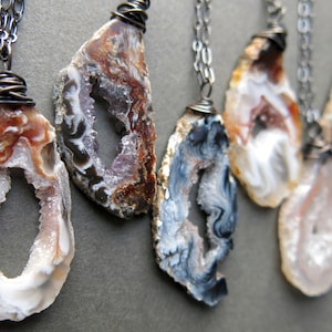May include: A collection of seven agate slice pendants, each with a unique colour and pattern, including brown, white, black and purple. Each pendant is wrapped in wire and hangs from a silver chain.