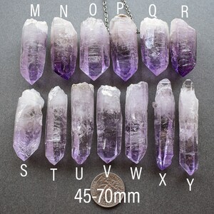 May include: Nine amethyst crystal points, labeled M through Y, measuring 45-70mm in length. The crystals are arranged in two rows on a gray surface.
