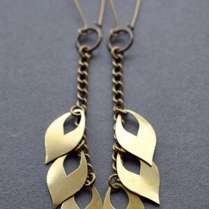 May include: A pair of gold dangle earrings with a chain and multiple leaf-shaped charms.