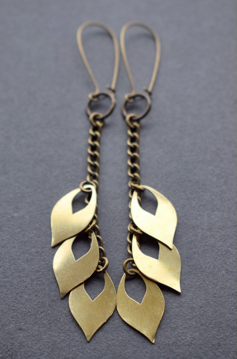 May include: A pair of gold dangle earrings with a chain and multiple leaf-shaped charms.