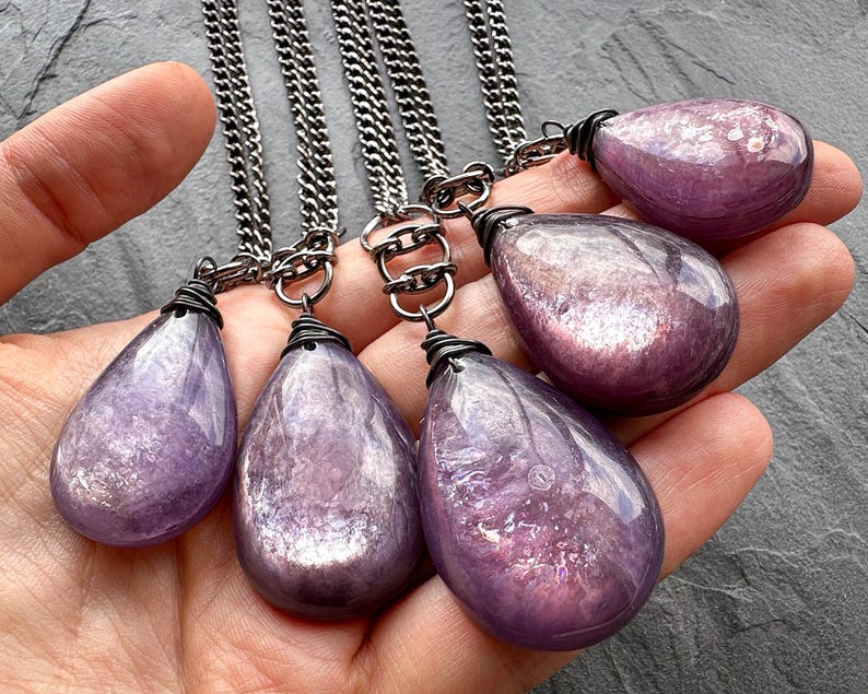 K&ouml;nnte beinhalten: Sechs tropfenf&ouml;rmige Amethyst-Anh&auml;nger an Silberketten. Jeder Anh&auml;nger hat eine andere Gr&ouml;&szlig;e und eine drahtumwickelte &Ouml;se. Die Amethyststeine haben eine durchscheinende, violette Farbe mit inneren Mustern. Die Ketten sind dunkelsilberfarben.