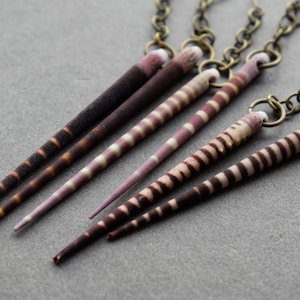 May include: A set of five striped, pointed, shell earrings with a bronze chain and clasp.