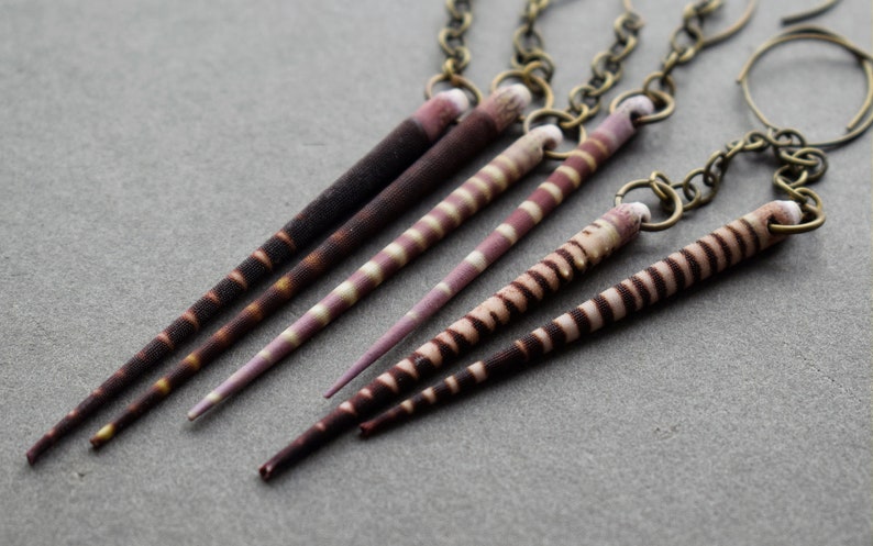 May include: A set of five striped, pointed, shell earrings with a bronze chain and clasp.