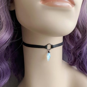 K&ouml;nnte beinhalten: Eine schwarze Choker-Kette mit einem silbernen Ring und einem klaren, schillernden Kristall-Anh&auml;nger.