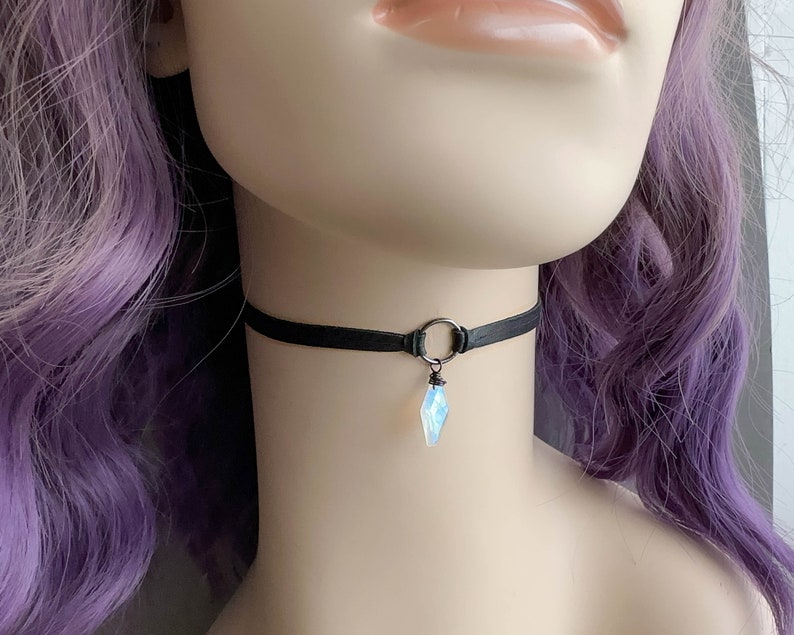K&ouml;nnte beinhalten: Eine schwarze Choker-Kette mit einem silbernen Ring und einem klaren, schillernden Kristall-Anh&auml;nger.