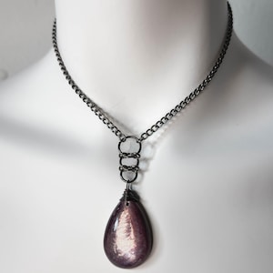 K&ouml;nnte beinhalten: Eine Halskette mit einer Kette aus Gunmetal mit einem tropfenf&ouml;rmigen Anh&auml;nger. Der Anh&auml;nger ist tiefviolett mit schillerndem Schimmer. Die Halskette hat eine Kette, drei Verbindungsringe und einen drahtumwickelten Anh&auml;nger.