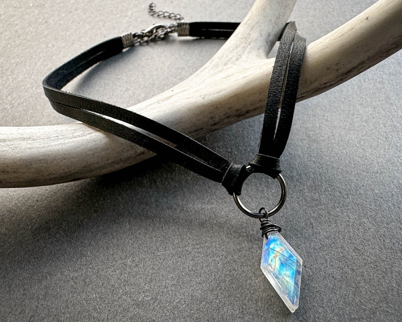 May include: A black leather choker necklace with a silver chain and a large iridescent gemstone pendant.