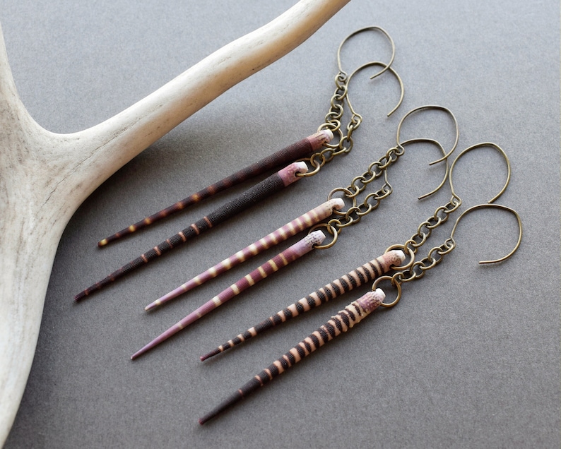 May include: A pair of earrings with long, striped, brown and pink shell pendants hanging from gold chains.