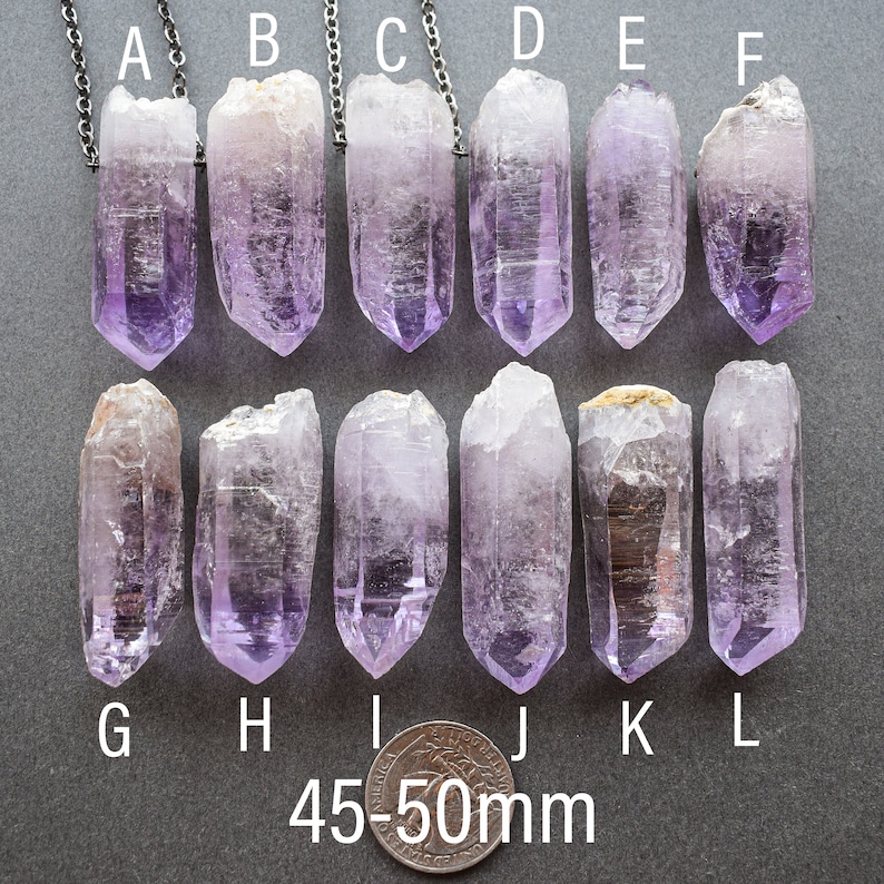May include: Twelve amethyst crystal points, labeled A through L, are arranged in two rows of six. The crystals are approximately 45-50mm in length and have a light purple hue.