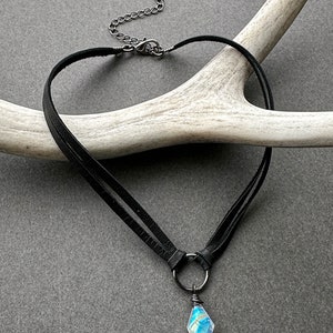 K&ouml;nnte beinhalten: Eine schwarze Lederkette mit einer silbernen Kette und einem regenbogenfarbenen Kristallanh&auml;nger.