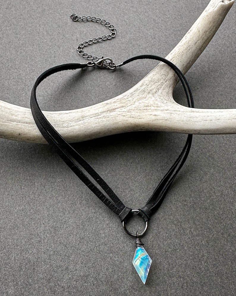K&ouml;nnte beinhalten: Eine schwarze Lederkette mit einer silbernen Kette und einem regenbogenfarbenen Kristallanh&auml;nger.