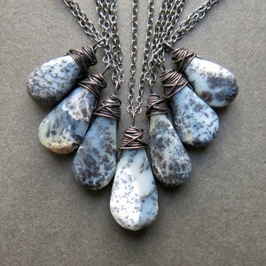 Puede incluir: Un conjunto de seis colgantes de &oacute;palo dendr&iacute;tico en forma de l&aacute;grima, cada uno envuelto en alambre de cobre oxidado oscuro y suspendido de una cadena de metal oscuro a juego. Las piedras tienen una base blanca lechosa con inclusiones negras.