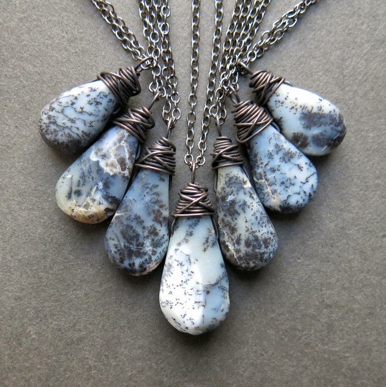 Puede incluir: Un conjunto de seis colgantes de &oacute;palo dendr&iacute;tico en forma de l&aacute;grima, cada uno envuelto en alambre de cobre oxidado oscuro y suspendido de una cadena de metal oscuro a juego. Las piedras tienen una base blanca lechosa con inclusiones negras.
