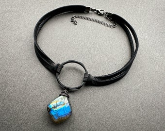 Könnte beinhalten: Eine schwarze Lederkette mit einer silbernen Kette und einem großen, schillernden blauen und goldenen Edelstein-Anhänger.