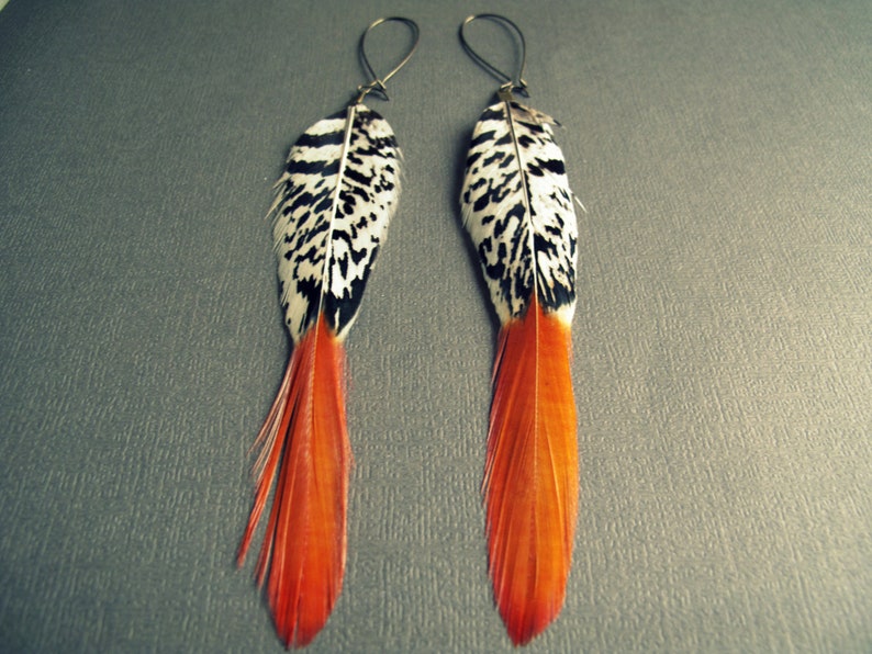 May include: A pair of long feather earrings with black and white patterned feathers and orange tips.