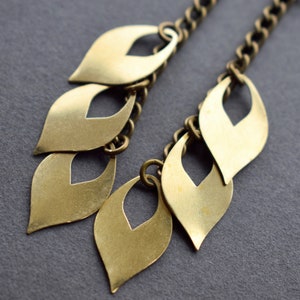 May include: Gold tone dangle earrings with a chain and multiple leaf-shaped charms.