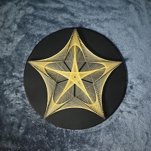 May include: A circular black wall art piece featuring a geometric star design created with thin yellow string. The string is wrapped around pins to form a complex, layered star pattern that radiates from the centre towards the outer edges.