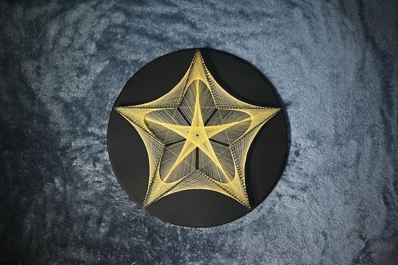 May include: A circular black wall art piece featuring a geometric star design created with thin yellow string. The string is wrapped around pins to form a complex, layered star pattern that radiates from the centre towards the outer edges.